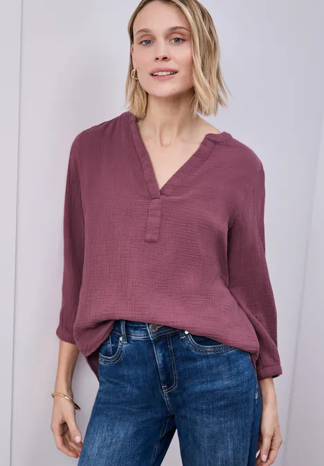 Eine Person trägt eine lose bordeauxrote Bluse mit V-Ausschnitt und dunkelblaue Jeans.